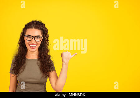 Laughing woman looking at camera et dirigés à l'écart avec pouce sur fond jaune Banque D'Images