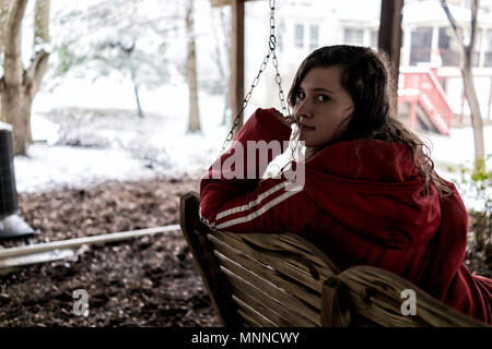 Gros plan du jeune femme happy smiling face sitting on swing sous terrasse en bois de chambre sur cour dans quartier avec la neige blizzard white stor Banque D'Images