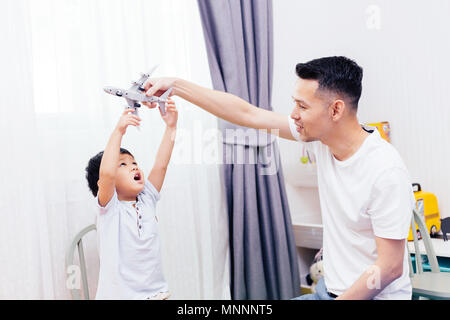 Curieux enfant regardant à l'avion jouet et jouer avec père. La famille asiatique jouant ensemble à la maison des jouets Banque D'Images