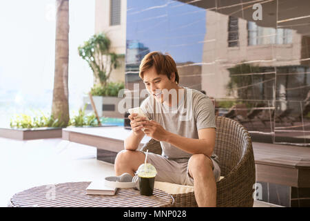 Journée ensoleillée d'été, joyeux sourire attrayant homme asiatique utilise le smartphone Banque D'Images