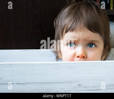 Close up of beautiful blue eyed baby enfant assis et de se cacher dans un fort curieusement à la recherche. Copier l'espace. Banque D'Images