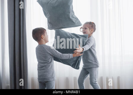 Petit garçon et fille ont organisé une guerre d'oreillers sur le lit dans la chambre à coucher. Vilains enfants battre à chaque autres oreillers. Ils aiment ce genre de jeu Banque D'Images