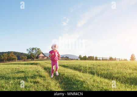 Cute little baby girl jouer dehors tôt le matin dans la pelouse et admirer les montagnes. Copie de l'espace pour votre texte Banque D'Images