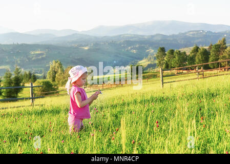 Cute little baby girl jouer dehors tôt le matin dans la pelouse et admirer les montagnes. Copie de l'espace pour votre texte Banque D'Images