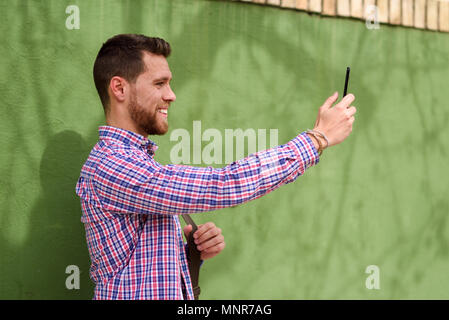 Jeune homme de prendre des photos avec son téléphone intelligent en contexte urbain. Les tenues de mec. Concept de vie. Banque D'Images