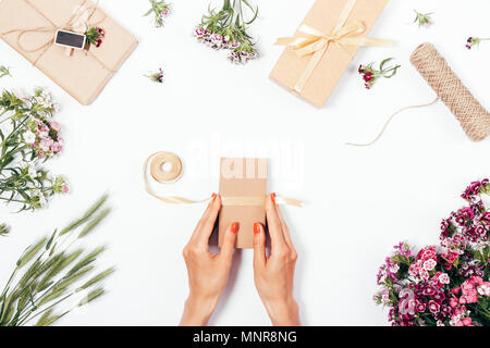 Processus de l'emballage des cadeaux et se préparer à la célébration, de mise à plat. Vue de dessus de la femelle les mains lient un ruban sur une boîte entre les bouquets, cadeaux et cordes de jute o Banque D'Images