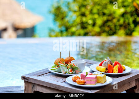 Service en chambre délicieux déjeuner des hamburgers, des fruits et des bonbons servis sur une table proche piscine Banque D'Images