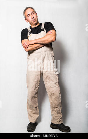 Mâle homme plombier spécialiste, ingénieur ou d'un constructeur en blanc sale minable vieux costume de travail, t-shirt noir et des bottes avec bras croisés l'article Banque D'Images