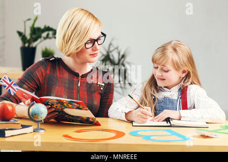 Kid girl réussie qui étudient le français langue avec elegant blonde enseignante, une table avec des livres et des lettres, des processus d'apprentissage en classe élégant blanc Banque D'Images