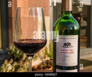 Une bouteille de vin rouge fine française, chanté du Sanglier 2014, Château de Fayolle, avec le vin en verre sur table d'extérieur dans le jardin au soleil du soir Banque D'Images