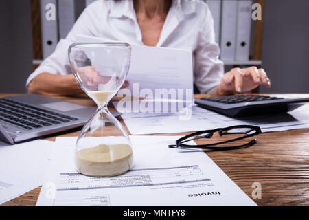 Close-up d'un sablier sur facture en face de Businesswoman Working On Document Banque D'Images