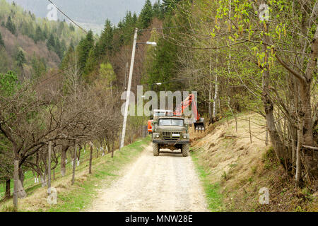 L'excavatrice élargit la route et charge les terres dans un camion dans les montagnes des Carpates, l'Ukraine. À l'extérieur. Plan d'ensemble. Banque D'Images