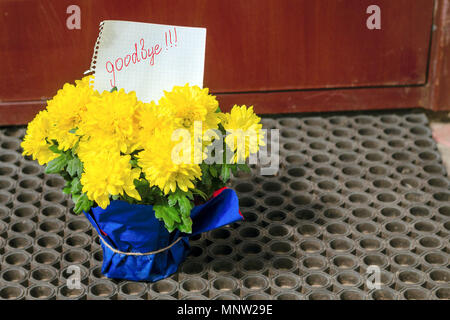 Une lettre sur un morceau de papier 'au revoir' est dans un bouquet de fleurs jaunes à l'entrée de la maison. La notion de séparation. Close-up. Banque D'Images