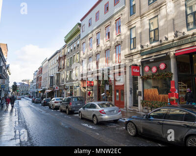 La rue commerciale dans le Vieux Québec -- l'hiver : une ligne de vieux bâtiments en brique et pierre, maintenant des boulangeries et des magasins, dans une rue pavée de la ville de Québec en hiver. Les voitures en stationnement sur un côté et les piétons à pied le trottoir. Banque D'Images