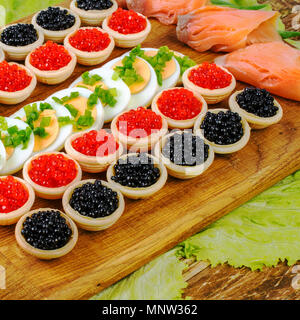 Des tartelettes avec du caviar rouge et noir, le saumon, la laitue et les oeufs. Sur une planche à découper. Concept d'aliment de luxe. Square. Close-up. Banque D'Images