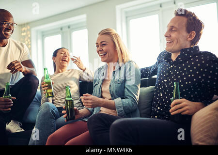 Groupe diversifié de laughing young businesspeople boire des bières tout en vous relaxant après travailler ensemble dans un bureau moderne Banque D'Images