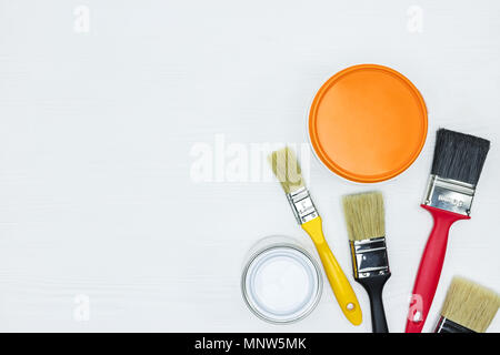 Des pots de peinture blanche et orange et jeu de balais sur le bureau en bois blanc vue plate. Banque D'Images