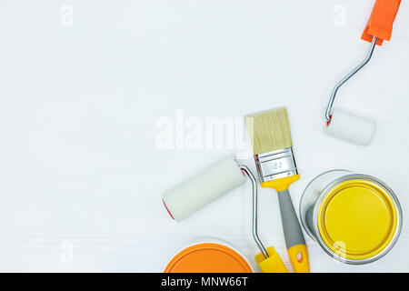 Rouleaux de peinture, pinceaux et boîtes de jaune et orange sur fond de bois peint blanc Banque D'Images