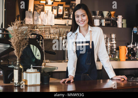 Asian female barista de porter un tablier jean place sa main sur le comptoir de bar et souriant au concept de service client,cafe,propriétaire démarrage d'entreprise. Banque D'Images