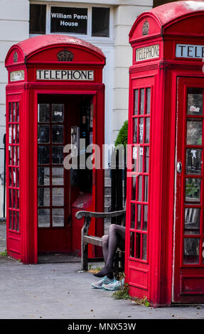 Femme assis sur un banc entre deux boîtes de téléphone rouge, changer ses chaussures, Londres, Angleterre, Royaume-Uni Banque D'Images