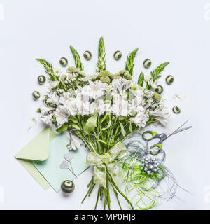 Beau bouquet de fête avec des fleurs vertes sur fond blanc 24 avec enveloppe et carte papier des maquettes, du ruban et des ciseaux, vue d'en haut. Vacances g Banque D'Images