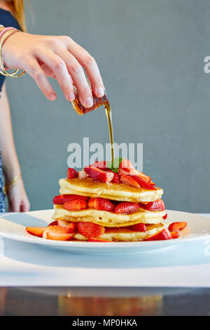 Woman pouring honey sur pile de crêpes aux fraises Banque D'Images