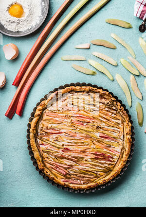 Gâteau à la rhubarbe . Tarte à la rhubarbe maison cuit sur fond bleu table de cuisine avec des ingrédients, vue du dessus. Cuisine de saison et la notion Banque D'Images