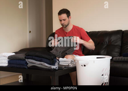 Bel homme folding laundry sur un canapé Banque D'Images