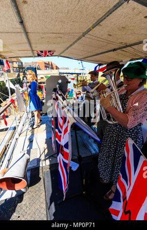 Salut à la 40s populaire événement nostalgique en Angleterre. La victoire de la bande de guerre et une femme sur scène chanteuse pont de bateau avec l'Union jack drapeaux. Banque D'Images