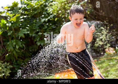 Jeune garçon jouant avec aspersion d'eau dans le jardin arrière