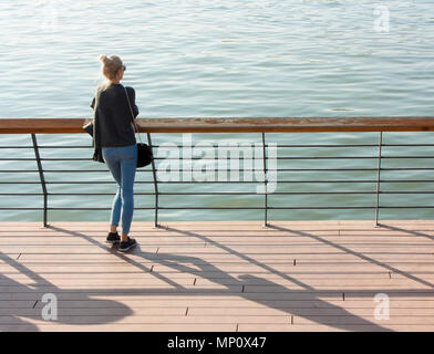 Belgrade, Serbie - 15 octobre 2017 : Young blonde woman standing on the river promenade se penchant sur les grilles et à la recherche à l'eau, de l'arrière Banque D'Images