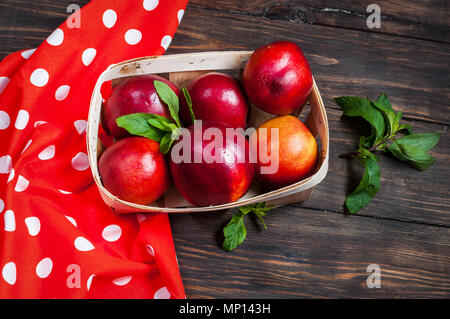 Petites nectarines mûres, couché dans un panier en osier sur fond de bois. Banque D'Images