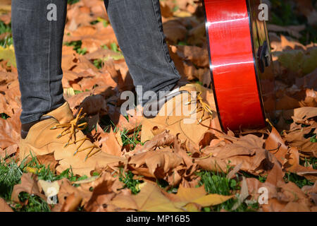 Pieds de jeune fille qui marche à travers les feuilles d'automne, falen holding guitare rouge Banque D'Images