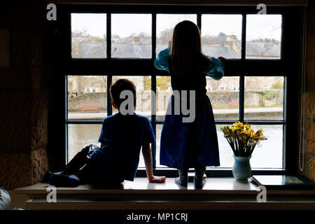 Frère (5 ans) et sa soeur (3 ans) était assis sur un rebord de fenêtre, silhouetté contre une fenêtre à guillotine avec la rivière Wye dans l'extérieur Bakewell