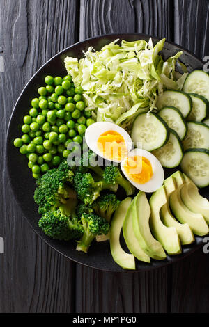 Vert sain alimentation : légumes frais avocat, pois, choux, concombre, brocoli et œufs durs gros plan sur une assiette. Haut Vertical Vue de dessus Banque D'Images