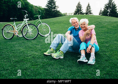 Happy senior couple est assis sur l'herbe, profiter le reste après la bicyclette. Stand des vélos à côté d'eux. Le repos actif des personnes âgées, Banque D'Images