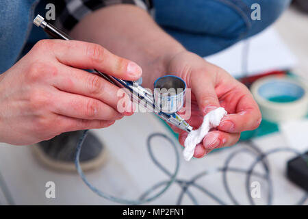 Close-up of a woman artist en jeans nettoie et prépare l'aérographe pour les travaux de peinture des murs. Banque D'Images