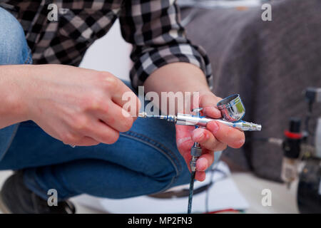 Close-up of a woman artist en jeans nettoie et prépare l'aérographe pour les travaux de peinture des murs. Banque D'Images