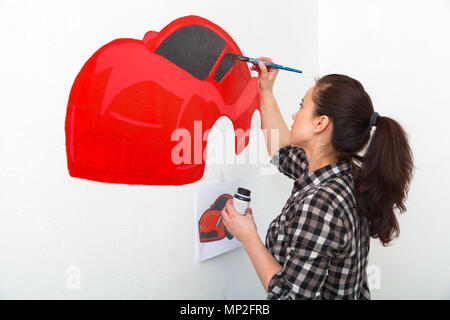 Jeune femme peintre et mère d'un enfant garçon s'appuie sur un mur blanc d'une belle voiture rouge dans une chambre d'enfants Banque D'Images