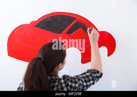 Jeune femme peintre et mère d'un enfant garçon s'appuie sur un mur blanc d'une belle voiture rouge dans une chambre d'enfants Banque D'Images