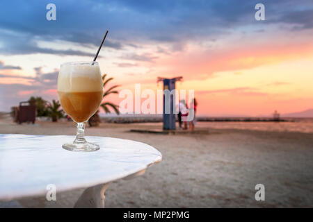 Un verre de freddo cappuccino café froid sur une plage au coucher du soleil contexte à Volos, en Grèce. Banque D'Images