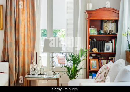 Détail d'un salon intérieur, de l'anglais - rustique avec des rideaux en bois, bibliothèque, des bougies et des persiennes en bois, lumière du jour. Banque D'Images