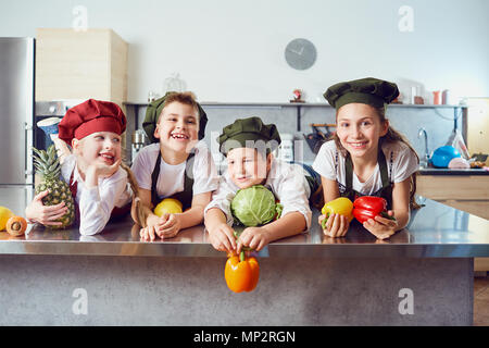 Les enfants drôles dans l'uniforme des cuisiniers sur la table dans les Banque D'Images