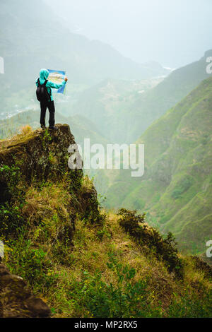 L'homme avec la carte restant sur le dessus de la roche en face d'une magnifique vue panoramique de hautes chaînes de montagne et vallée verdoyante. Banque D'Images