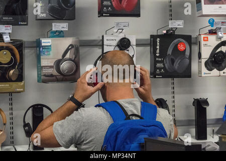 Un homme portant un t-shirt dans un magasin de détail à l'essai ou d'analyse portant casque tour d'oreille. L'homme écoute de musique portant des casques ou écouteurs. Banque D'Images