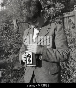 Années 1950, historiques, les écolier en extérieur dans un jardin à l'aide d'un 'réflexe' Brownie Kodak film photographique appareil photo. Cet appareil a été fabriqué en Angleterre par Kodak Ltd de 1946 à 1960. Comme on peut le constater, à l'utiliser, on regarda le viseur et tiendra la caméra à hauteur de la taille. Banque D'Images