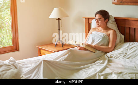 Girl reading gros livre au lit. Une femme avec réserve en chambre Banque D'Images