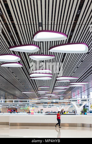 Une femme portant une chemise rouge passe devant un comptoir au terminal 4 de l'aéroport de Changi. Singapour. Banque D'Images