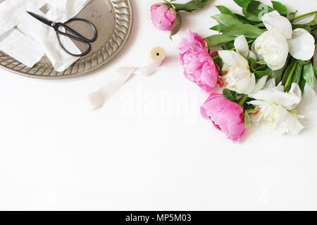 Stock photo style. Table d'anniversaire de mariage féminin ou la composition avec bouquet floral. Fleurs de pivoines blanches et roses, old vintage ciseaux, plateau d'argent et de rubans de soie. Arrière-plan blanc. Banque D'Images