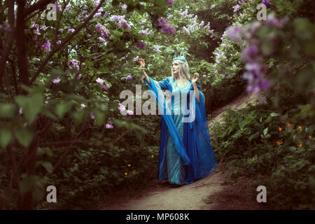 Jeune elfe femme marche dans une forêt féerique parmi les buissons de lilas. Banque D'Images